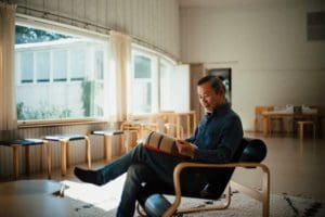 A man is sitting and reading in a designer chair inside a large and spacious room of the Aalto studio.