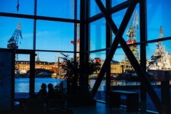 Sunny Hietalahti docks viewed through Hotel Clarion's tall windows. The interior is almost silhouetted entirely meaning only the cranes, ships and buildings of Hietalahti can be seen clearly.