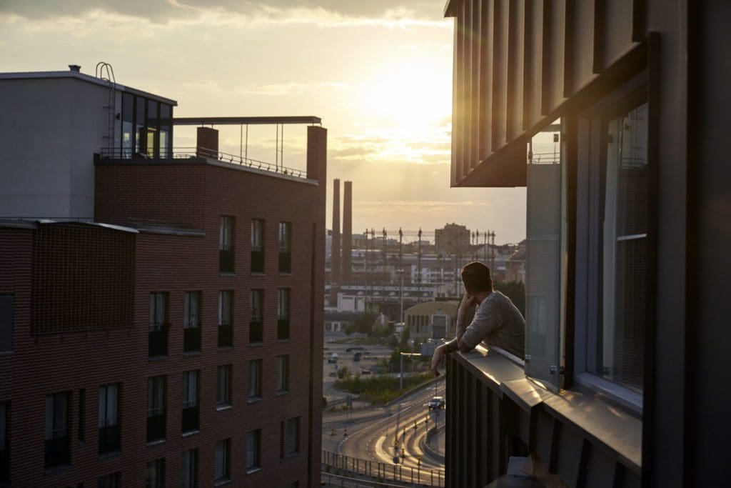 A man admires the sunset in Kalasatama, looking out from their apartment over the cityscape ahead.