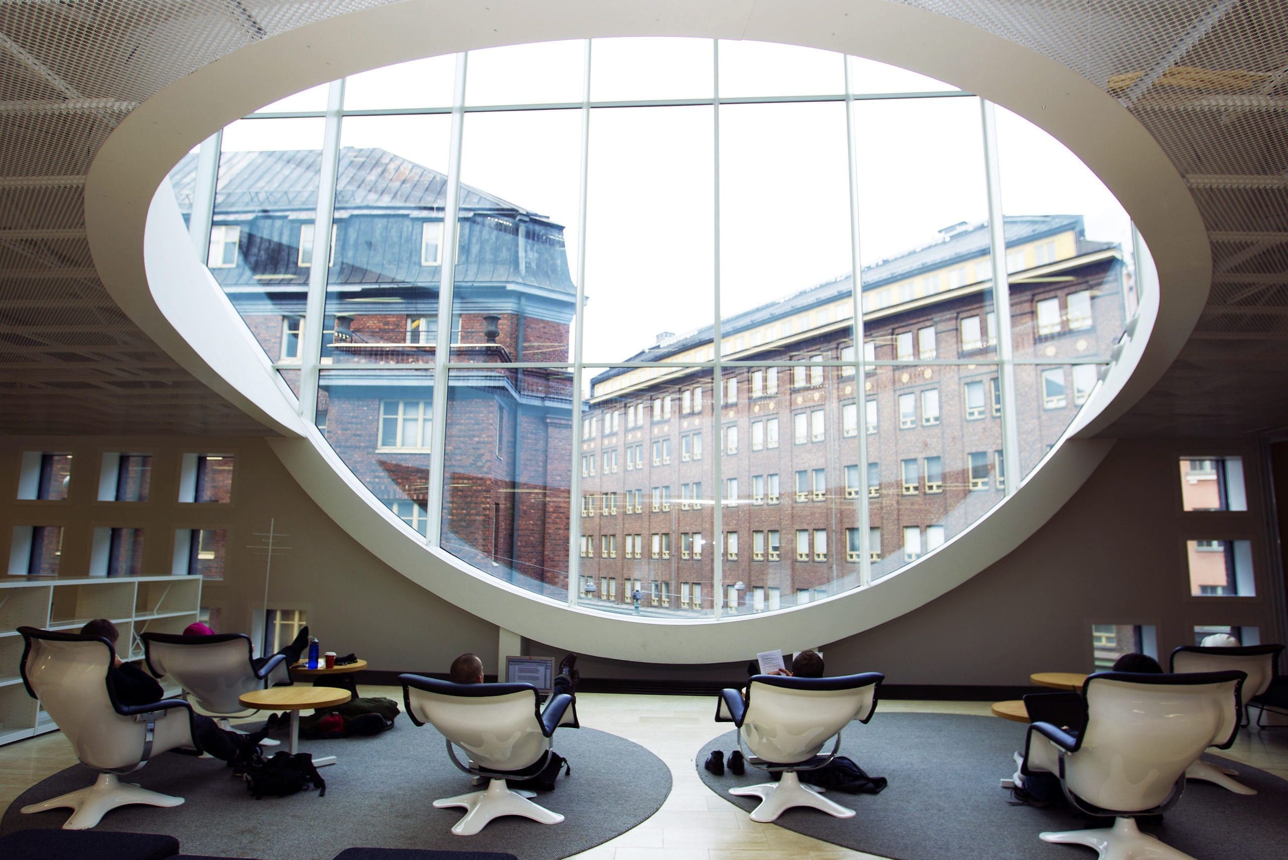 Viewed from behind and looking out through the huge window at Kaisa library, students sit, kickback and read.