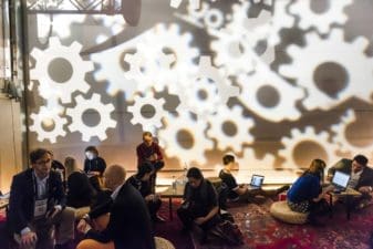 At Slush, in a tall room and against the backdrop of dozens of white cog wheels projected onto the far wall, a group of professionals sit on cushions at low tables discussing.