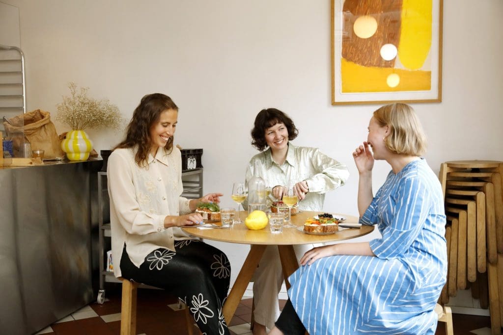 Three women chatting and smiling whilst sitting and enjoying lunch in a cafe.