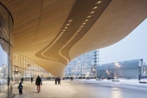 Standing underneath Oodi's outdoor front structure and with Kiasma in the distance to the right, Oodi's wooden roof sweeps in a curve like a wave, twisting to meet the ground many metres away.