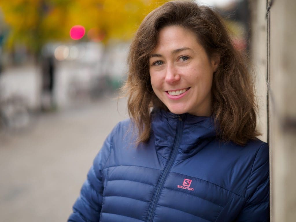 Sophie Winwood, 90 Day Finn 2021 participant and Investment Principal at Anthemis Group, smiles toward the camera whilst leaning against a wall on an autumnal Helsinki city street.