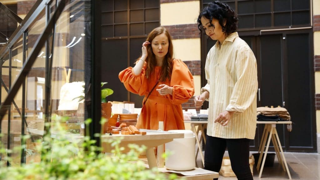 Two women stand chatting while browsing hand crafted products at the Glasshouse in Helsinki.