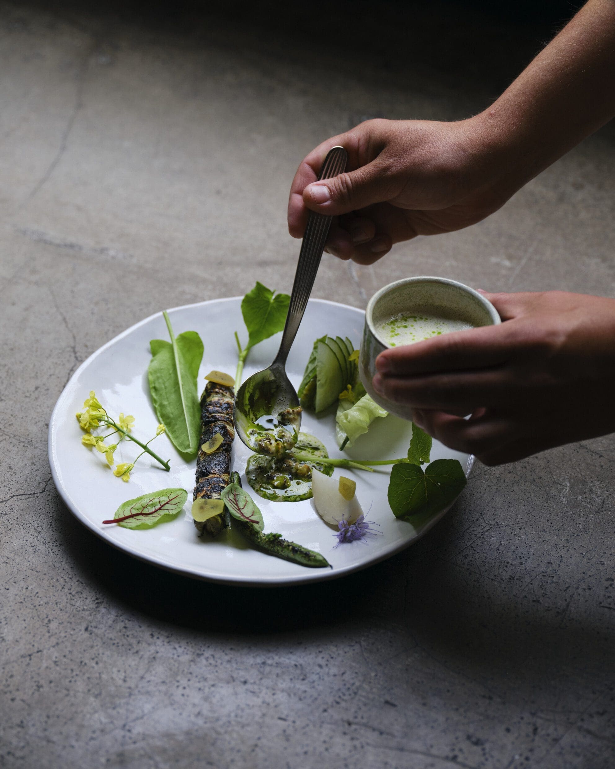 elicacy from restaurant Grön - Leek & pike "Roast", herbs from the Grön farm, grilled butter, mussel broth and parsley oil. Presented by Badass Food Stories in their piece, Farm-to-fork at Michelin-star restaurant Grön in Helsinki.