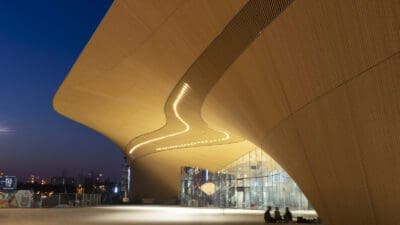 The wooden curves of the exterior of the Central Library Oodi at night.