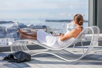 Woman lying in a sun lounger next to a large window at Clarion Hotel overlooking the harbour in the sunshine
