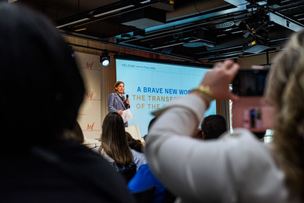 Woman presenting on stage behind an audience taking a photo