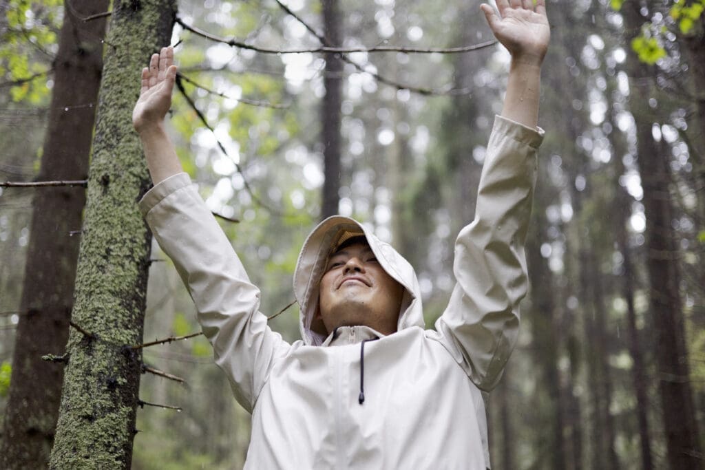 Man with his arms up in peaceful embrace of the falling rain deep in the Finnish woods