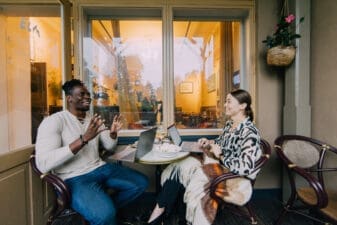 Two people discussing animatedly and sitting at a restaurant table with laptops in Helsinki.